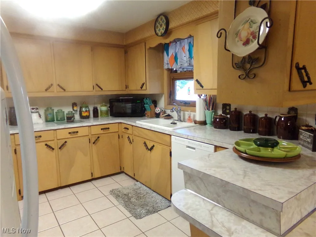 Kitchen featuring light countertops, light tile patterned floors, black microwave, dishwasher, and brown cabinets