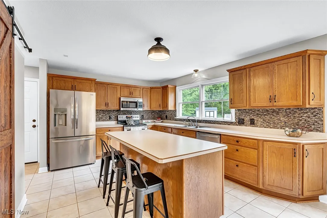Kitchen with stainless steel appliances, light tile patterned floors, a breakfast bar, and light countertops