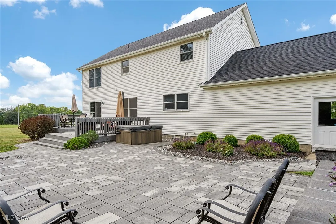 Rear view of property featuring a hot tub, roof with shingles, a patio, and a wooden deck