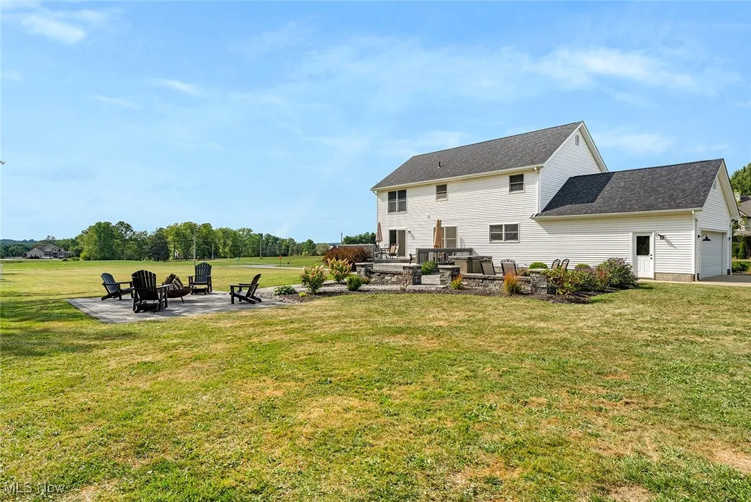 Rear view of house featuring a patio, an attached garage, a lawn, and an outdoor fire pit