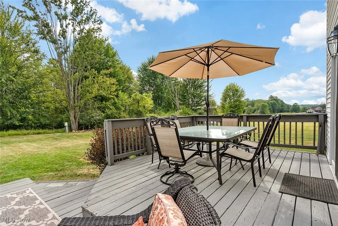 Wooden terrace featuring a yard, outdoor dining area, and view of wooded area