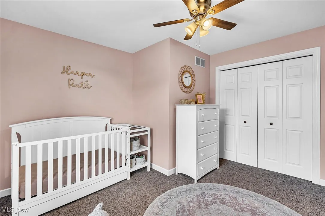 Bedroom with carpet flooring, a crib, ceiling fan, and a closet