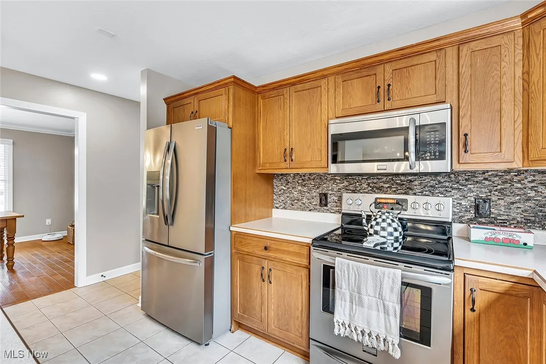 Kitchen featuring stainless steel appliances, light countertops, brown cabinetry, and recessed lighting