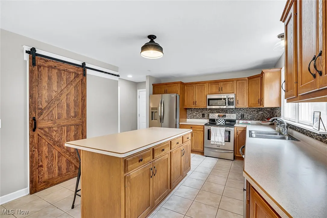 Kitchen with backsplash, light tile patterned floors, stainless steel appliances, and brown cabinetry