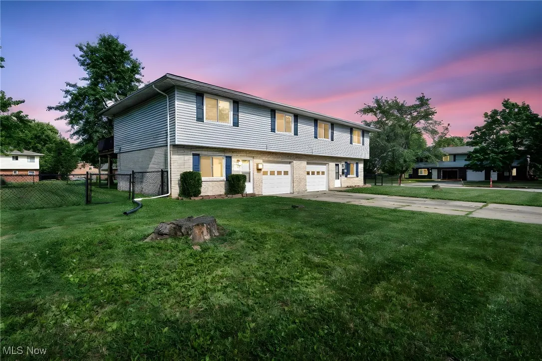 Romantic view of this Colonial duplex featuring concrete driveway, brick siding, and an attached garage