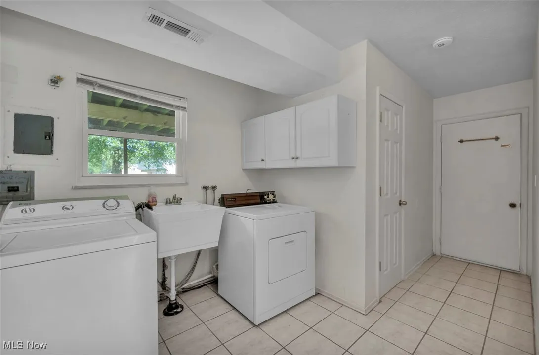 Laundry room with washing machine and clothes dryer, light tile patterned flooring, and cabinet space