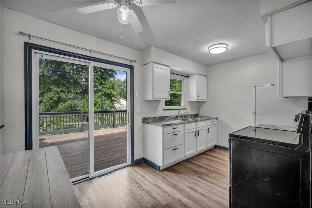 Eat-in Kitchen with sliding doors to deck; electric stove, light lvp flooring, white Shaker cabinets, and ceiling fan