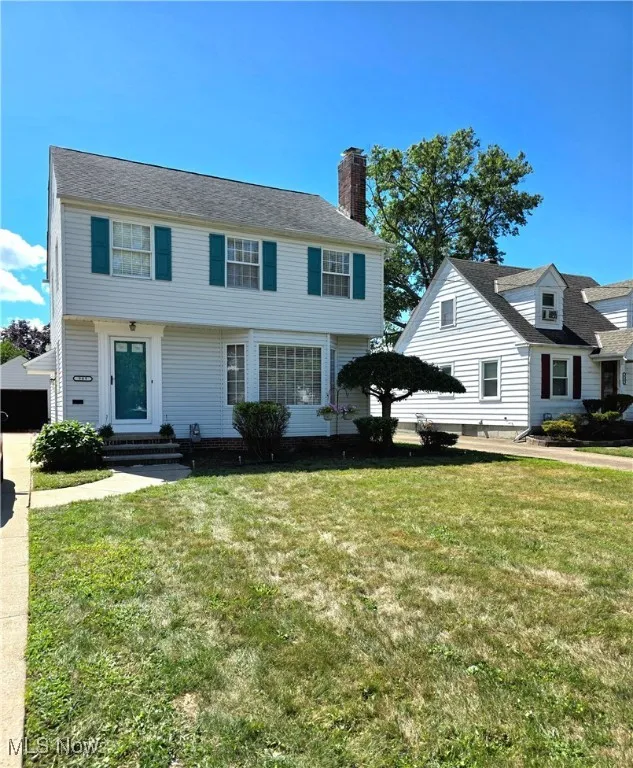 Colonial inspired home featuring a chimney, a front yard, and a detached garage