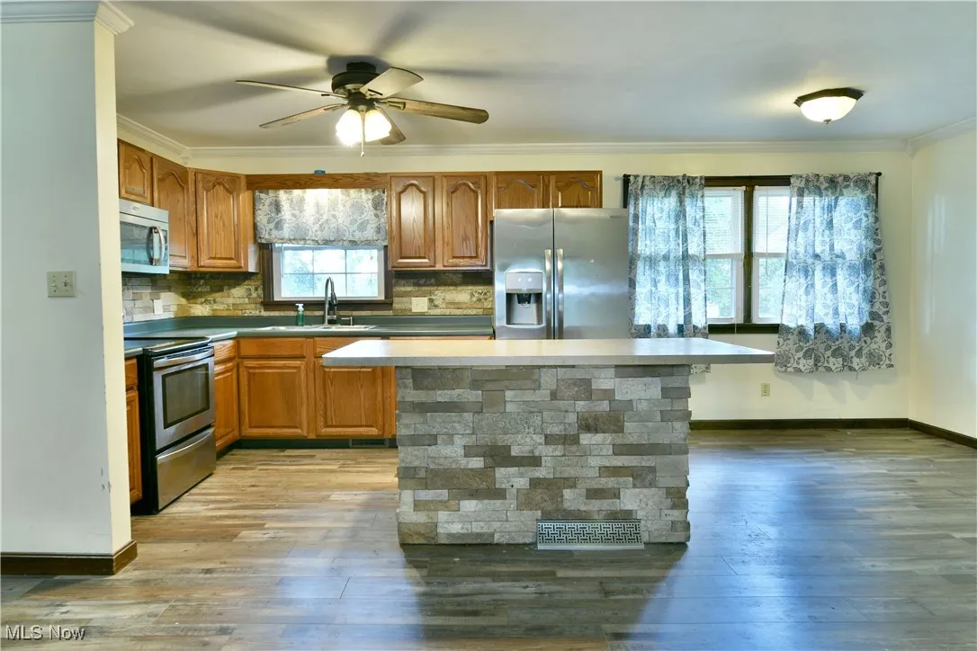 Kitchen with stainless steel appliances, backsplash, a center island, ornamental molding, and brown cabinetry