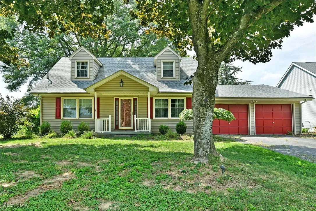Cape cod house with roof with shingles, an attached garage, covered porch, a front yard, and driveway