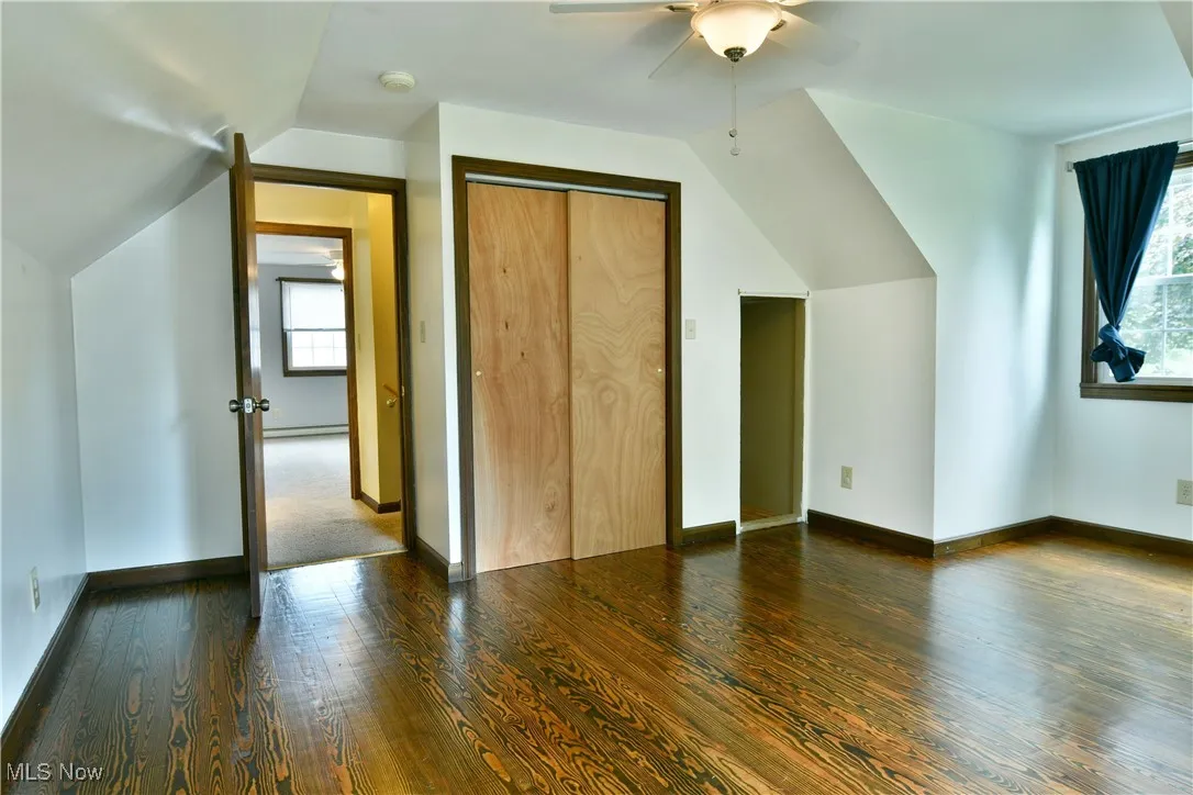 Additional living space with plenty of natural light, dark wood-type flooring, vaulted ceiling, ceiling fan, and a baseboard radiator