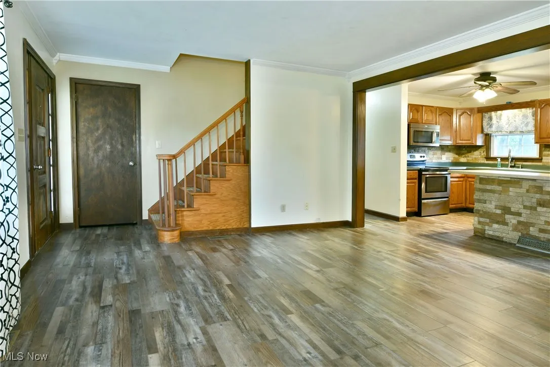 Kitchen featuring ornamental molding, stainless steel appliances, dark wood-style flooring, brown cabinets, and decorative backsplash