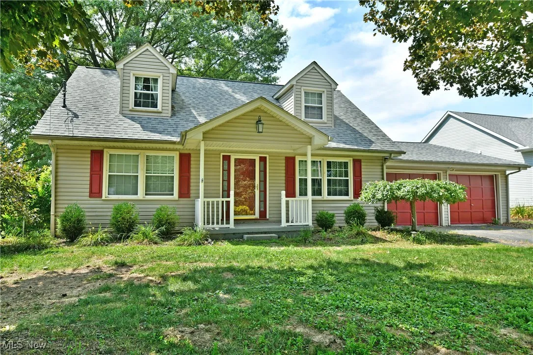 Cape cod house with roof with shingles, a porch, an attached garage, driveway, and a front lawn