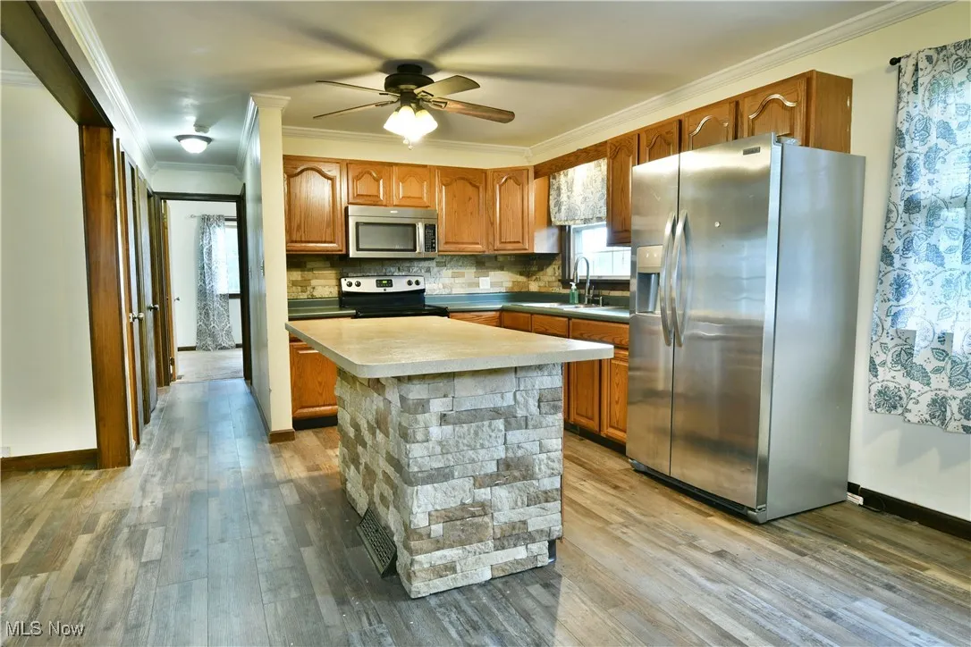 Kitchen featuring stainless steel appliances, crown molding, light wood-type flooring, light countertops, and brown cabinetry