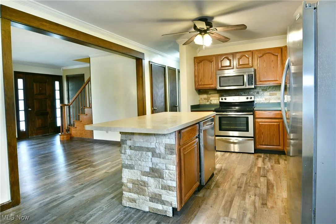 Kitchen with brown cabinets, stainless steel appliances, crown molding, backsplash, and light wood finished floors