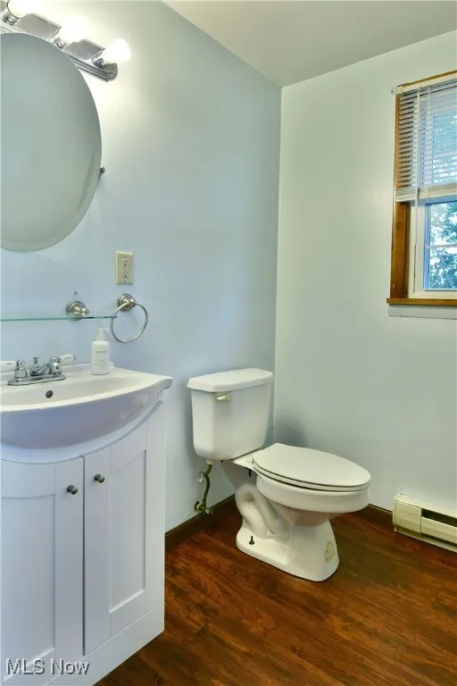 Half bathroom with dark wood-style flooring, a baseboard radiator, and vanity