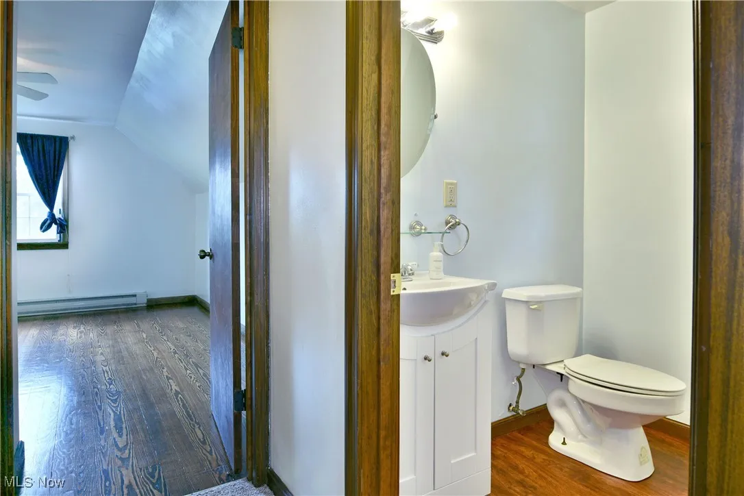 Bathroom featuring dark wood-style floors, vanity, a baseboard radiator, vaulted ceiling, and ceiling fan