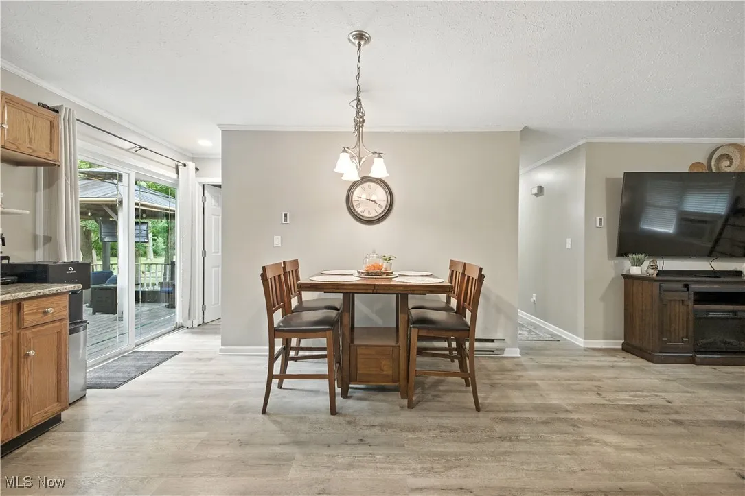 Dining room with ornamental molding, light wood-style floors, a textured ceiling, and a chandelier