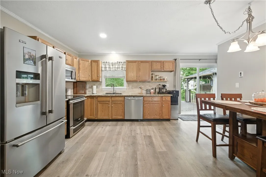 Kitchen with stainless steel appliances, backsplash, light wood-type flooring, crown molding, and pendant lighting