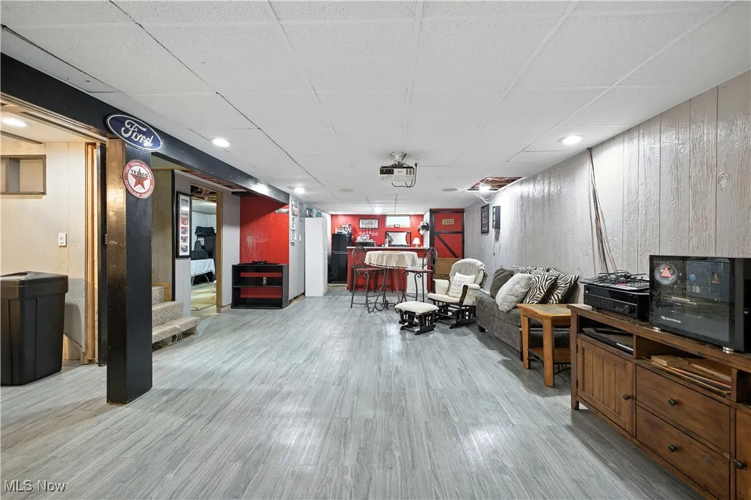 Living area with a drop ceiling, a dry bar, light wood-style floors, and wooden walls
