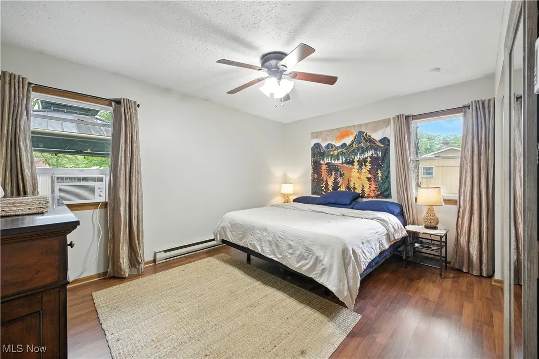 Bedroom featuring wood finished floors, a baseboard radiator, a textured ceiling, a ceiling fan, and cooling unit