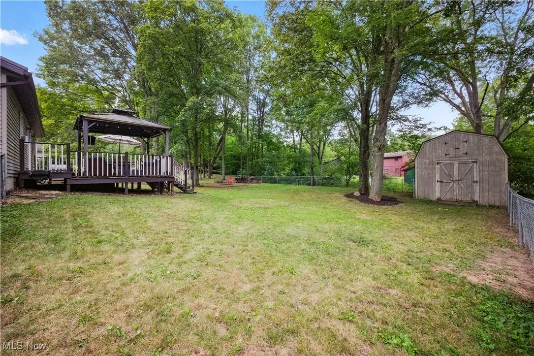Fenced backyard featuring a gazebo, a wooden deck, a storage unit, and view of scattered trees
