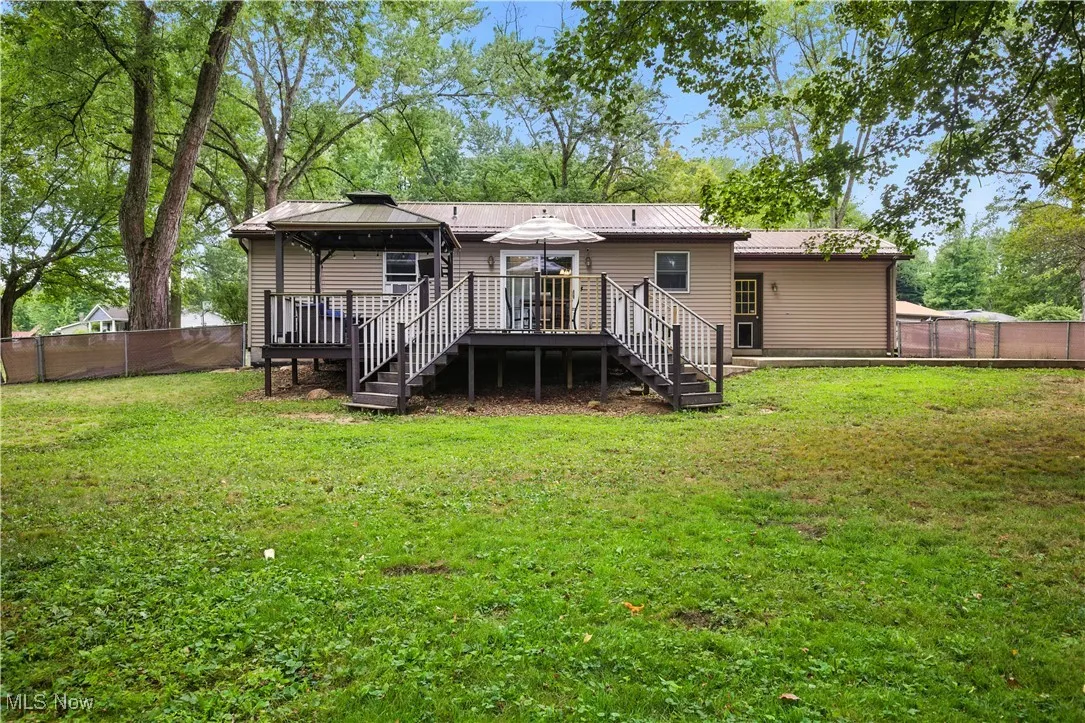 Rear view of house featuring a gazebo, stairs, a fenced backyard, a wooden deck, and a metal roof