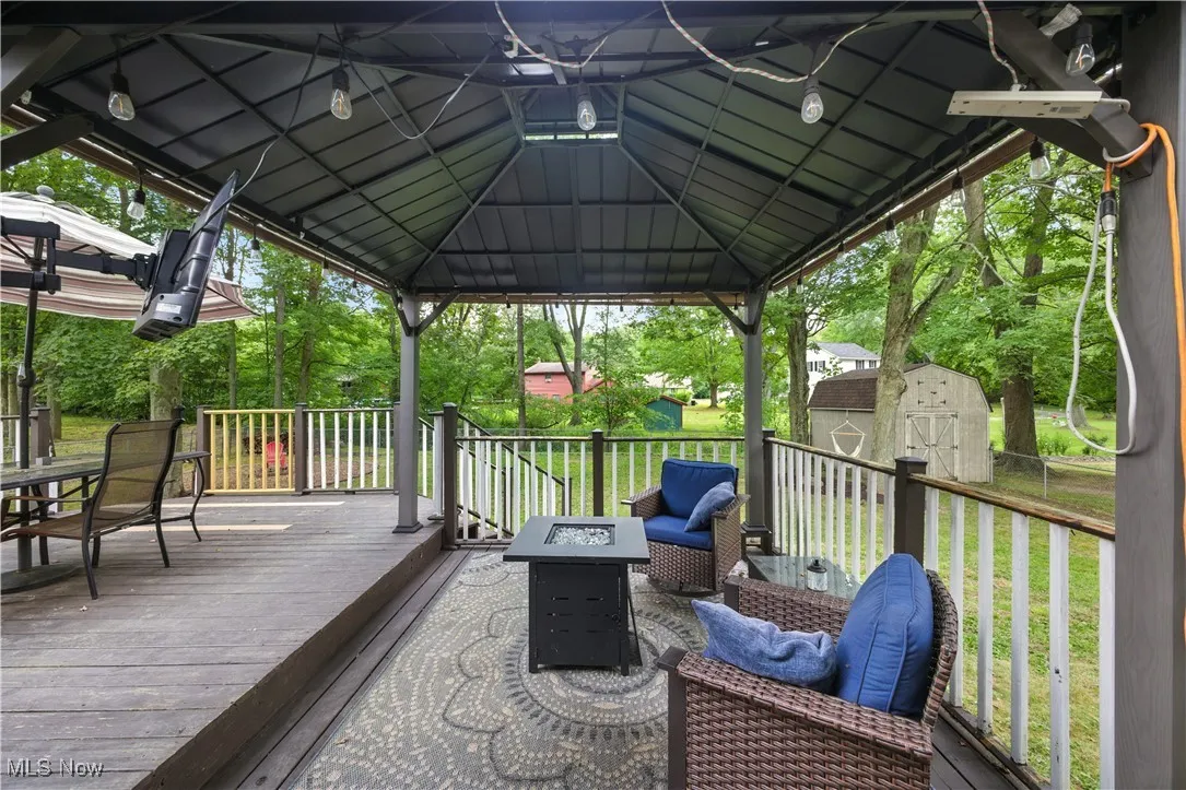 Wooden deck with a storage shed, a gazebo, outdoor dining space, a lawn, and view of wooded area
