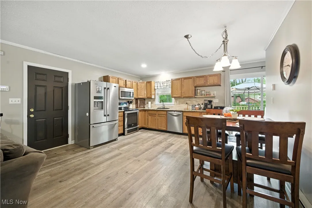 Kitchen featuring appliances with stainless steel finishes, crown molding, a chandelier, light wood-style floors, and decorative backsplash