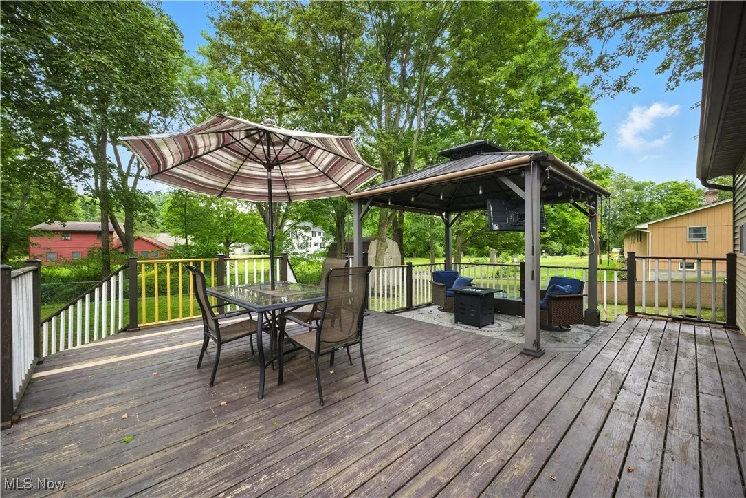 Wooden terrace featuring a gazebo, outdoor dining area, and a grill