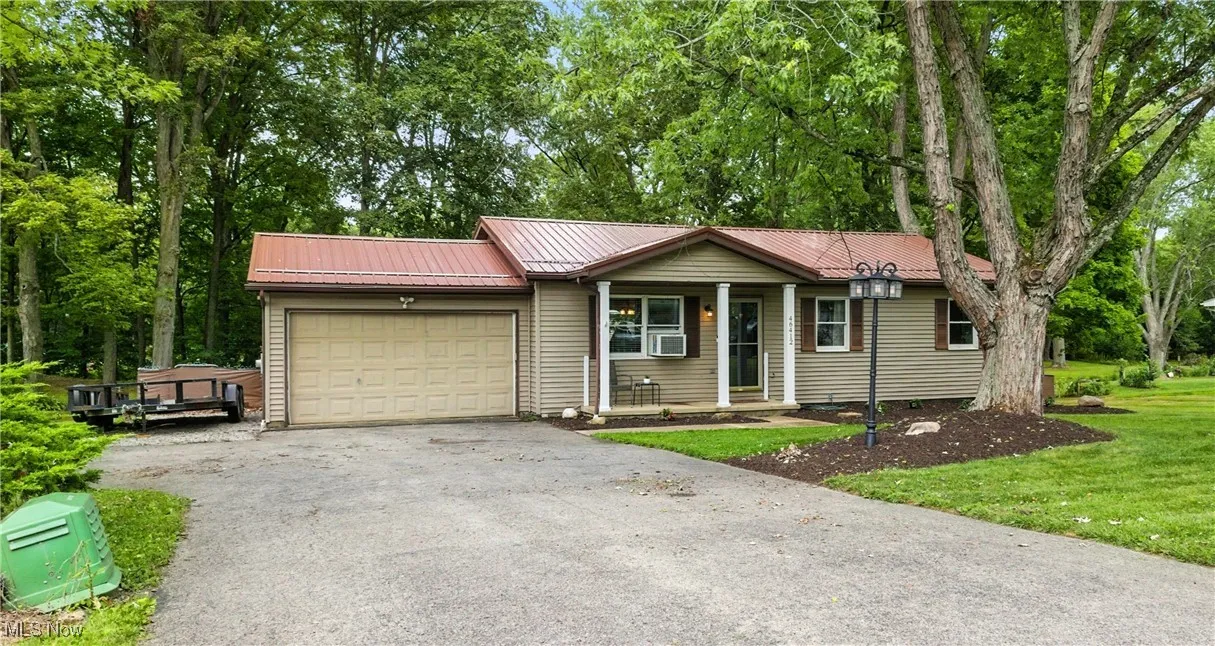 Ranch-style house featuring a garage, asphalt driveway, a porch, a metal roof, and a front yard