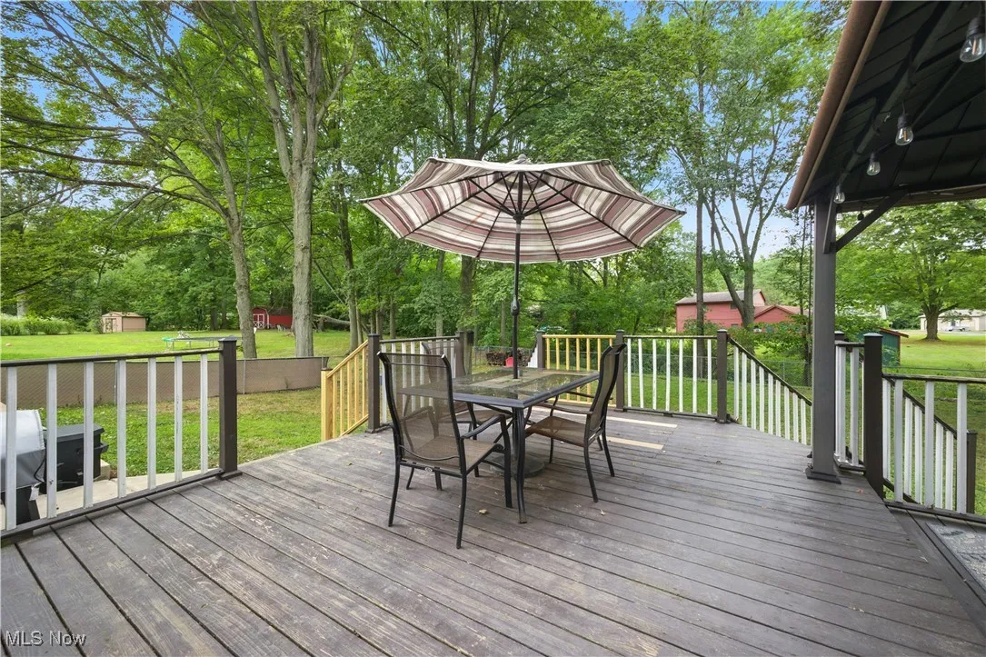 Deck with outdoor dining space, a lawn, view of scattered trees, and an outdoor structure