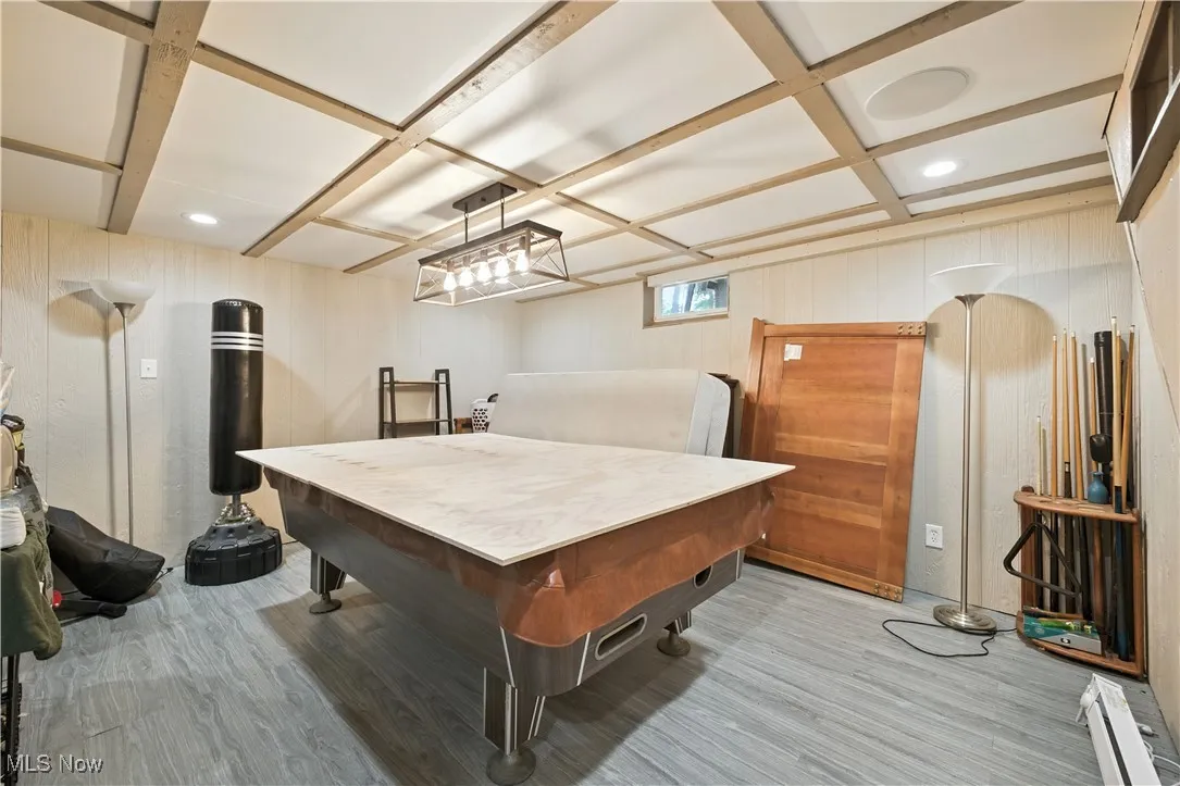 Rec room featuring light wood-type flooring, wooden walls, coffered ceiling, beamed ceiling, and baseboard heating