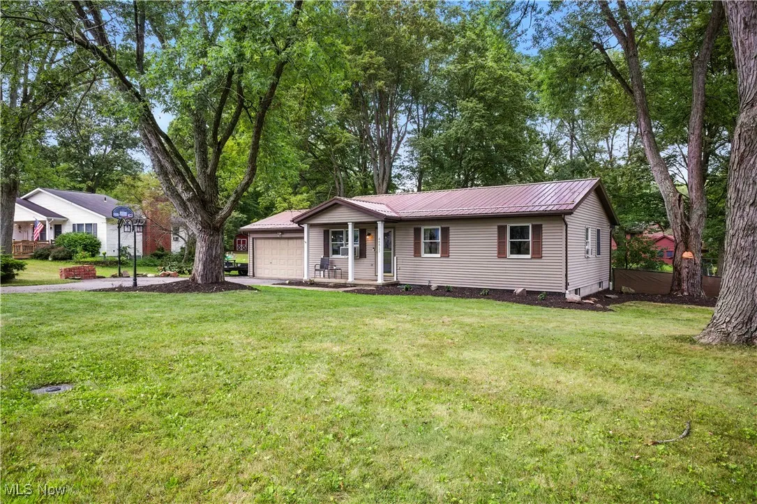 Single story home featuring a metal roof, a front yard, an attached garage, and view of scattered trees