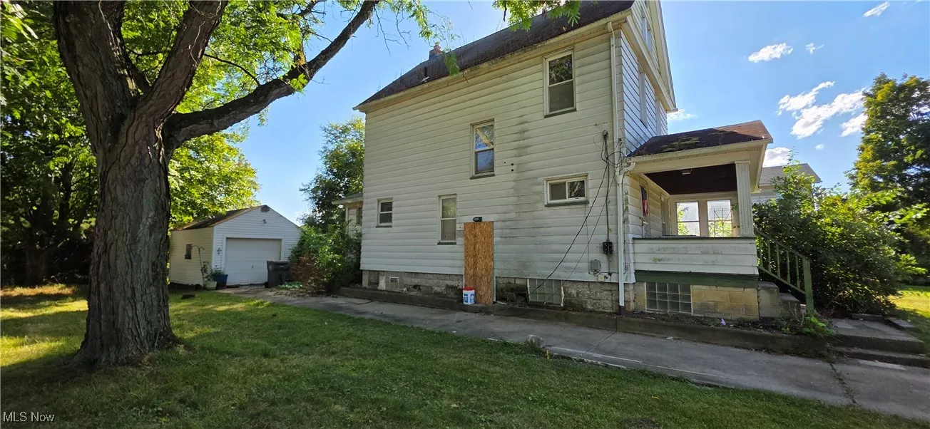 Back of property with a detached garage, an outdoor structure, a yard, and driveway