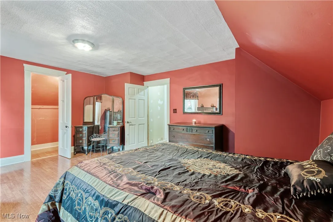 Bedroom with a textured ceiling, wood finished floors, and lofted ceiling