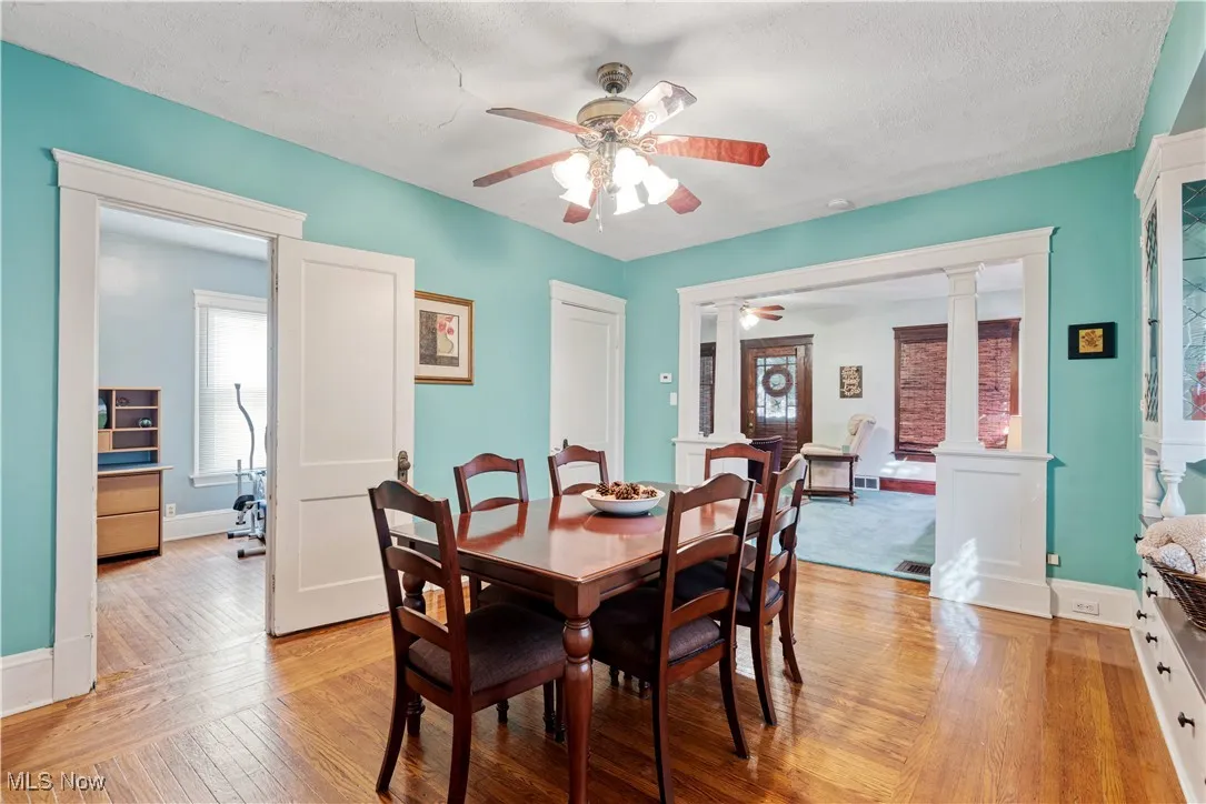 Dining area featuring decorative columns, light wood-style flooring, a ceiling fan, and a textured ceiling