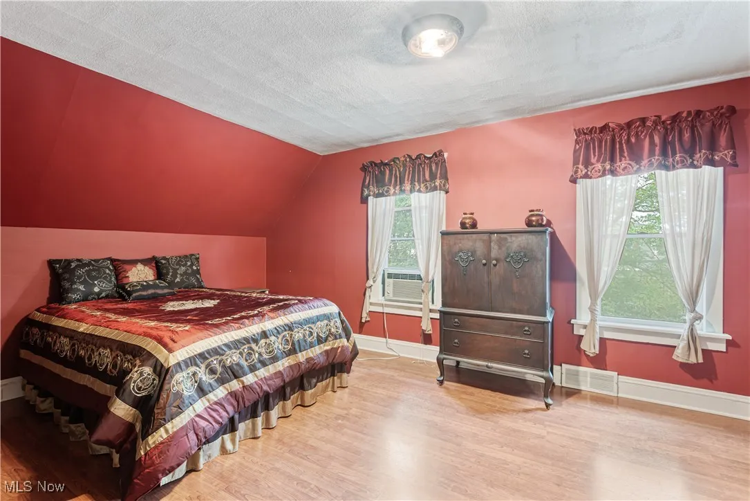 Bedroom with vaulted ceiling, light wood-type flooring, a textured ceiling, and cooling unit