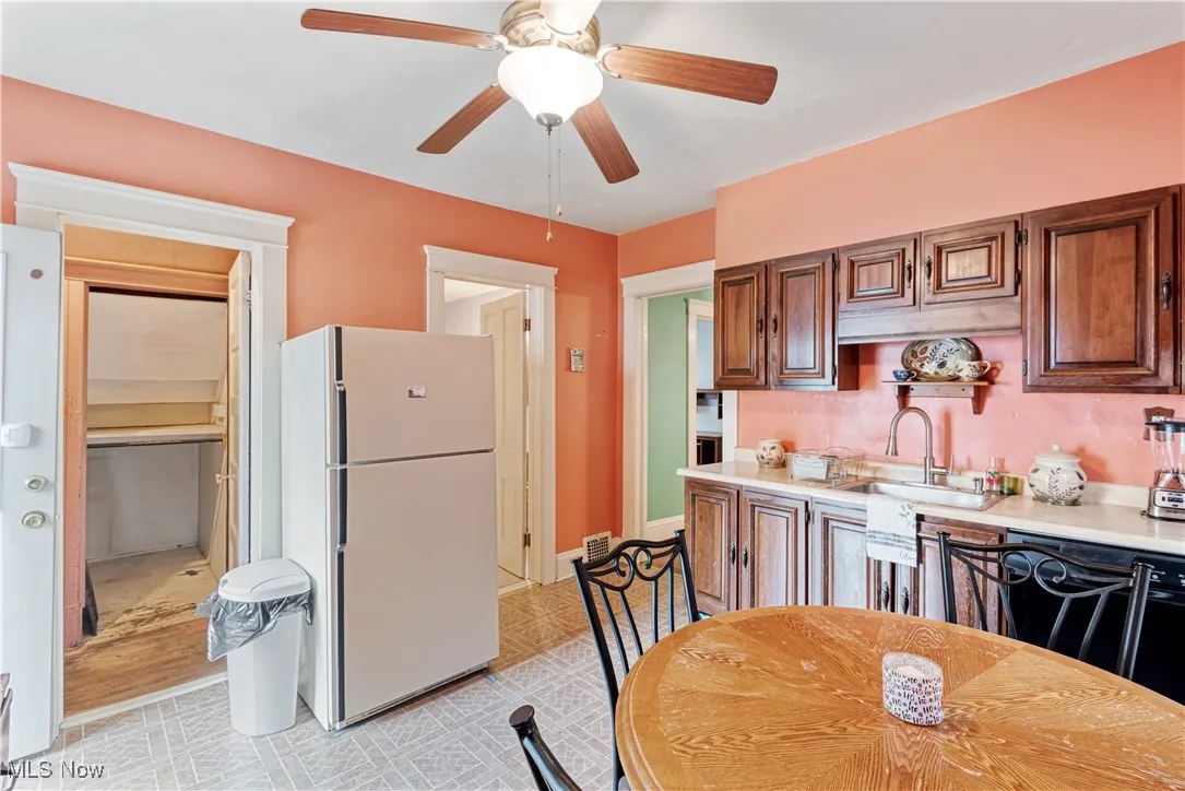 Kitchen with freestanding refrigerator, dishwasher, ceiling fan, brown cabinets, and light flooring
