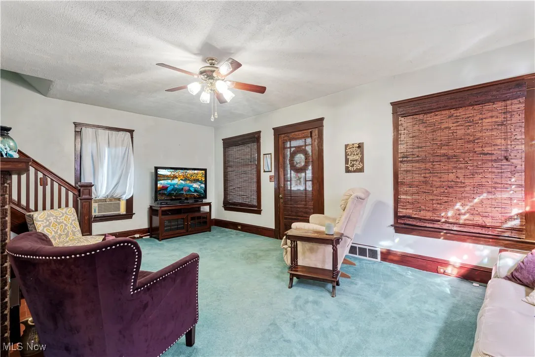 Living room with carpet, a textured ceiling, a ceiling fan, and stairway