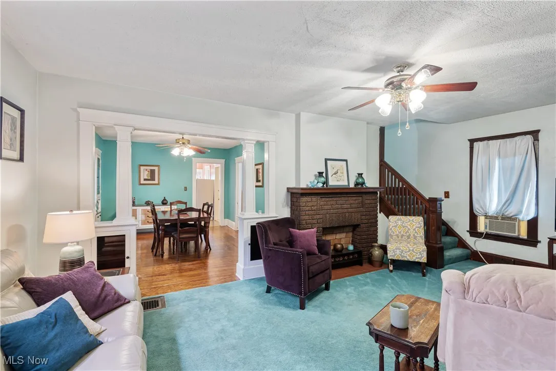 Living room featuring a ceiling fan, ornate columns, a textured ceiling, stairs, and a fireplace