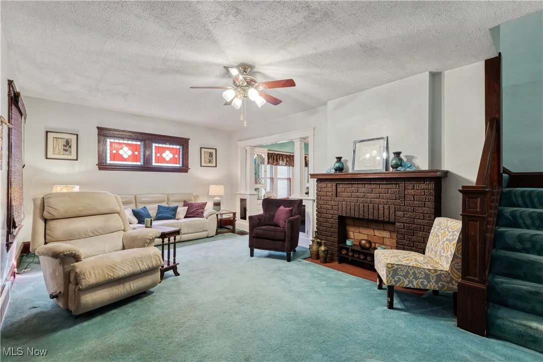 Living room featuring stairway, carpet floors, a textured ceiling, a ceiling fan, and a fireplace