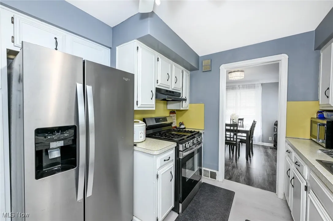 Kitchen featuring stainless steel appliances, white cabinets, light countertops, light wood-style flooring, and under cabinet range hood