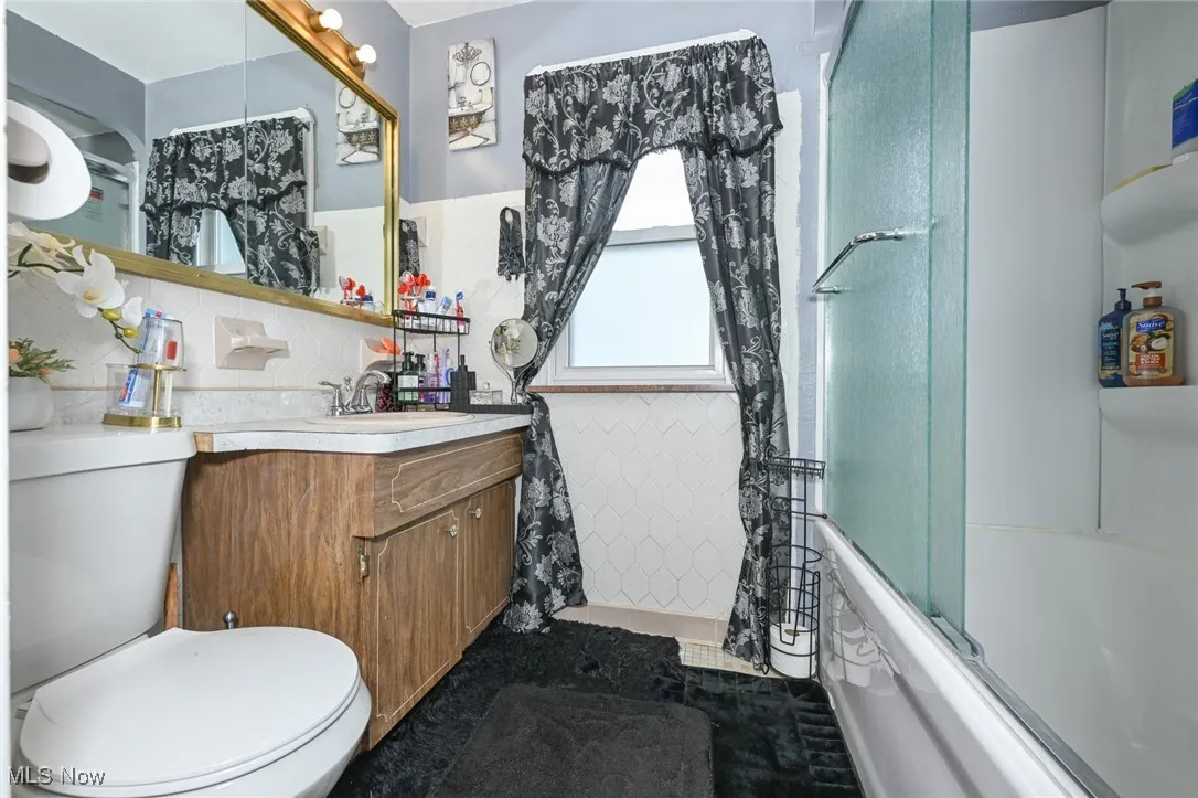 Full bath featuring tile walls, vanity, and combined bath / shower with glass door