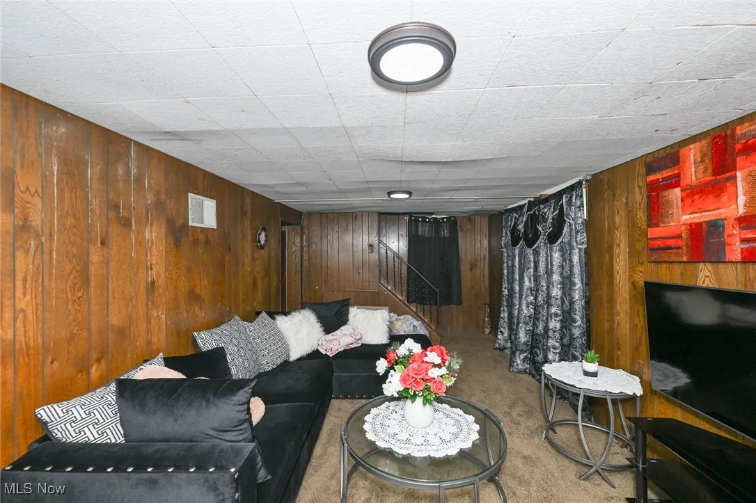 Living room featuring wooden walls, carpet floors, and stairway