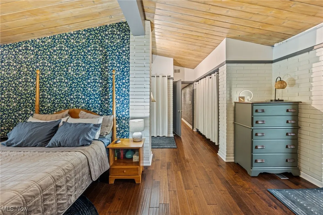 Bedroom with dark wood-style flooring, wooden ceiling, and brick wall
