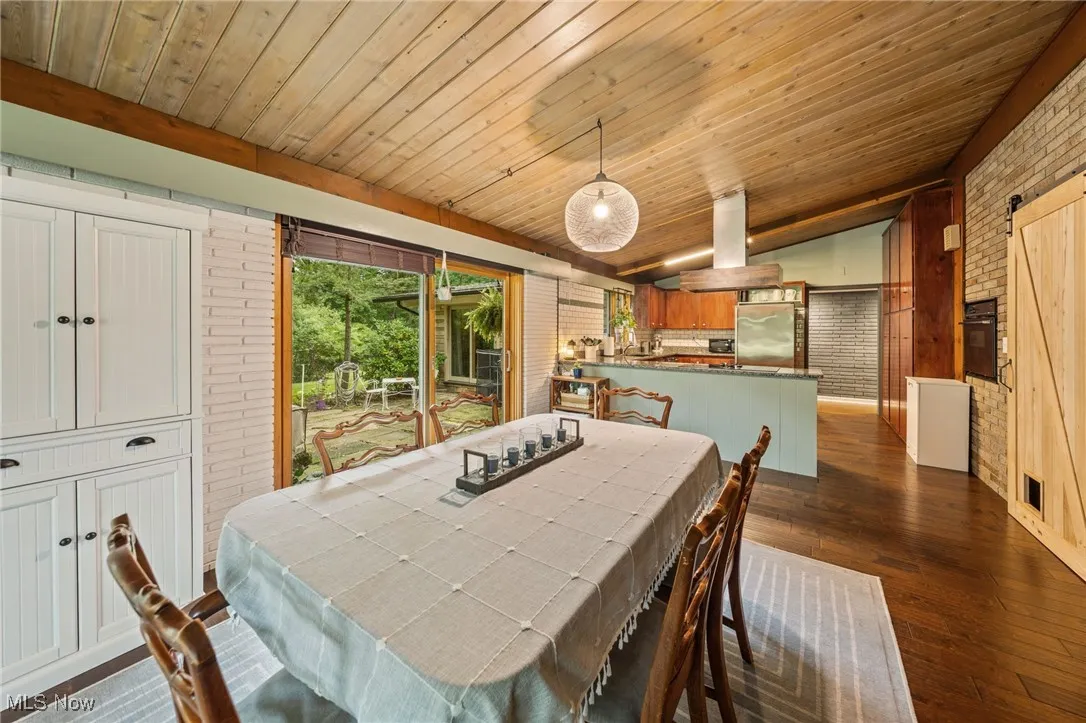 Dining room featuring brick wall, a barn door, dark wood-type flooring, lofted ceiling, and wooden ceiling