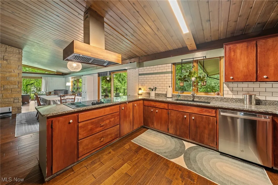 Kitchen with a peninsula, dishwasher, dark stone countertops, wall chimney exhaust hood, and a wooden ceiling with exposed beams