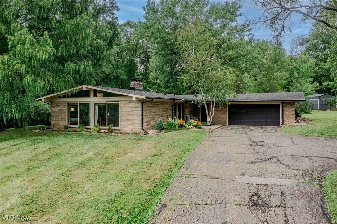 View of front of property featuring a garage, asphalt driveway, a front lawn, a chimney, and stone siding