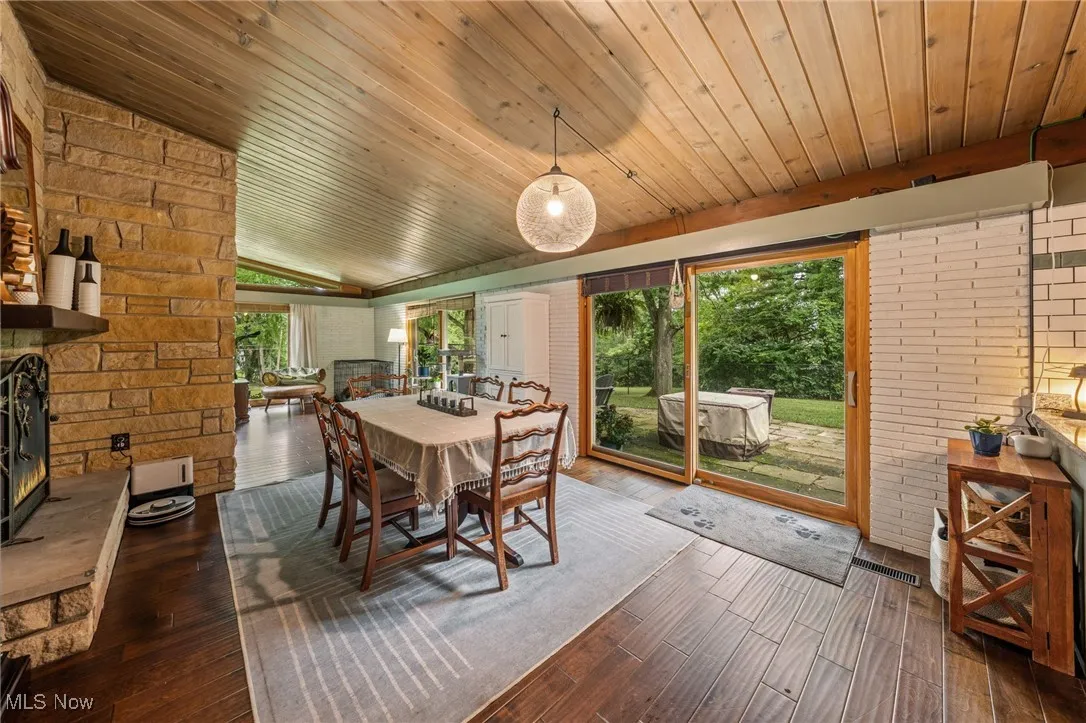 Dining room with brick wall, lofted ceiling, dark wood-style flooring, and a stone fireplace